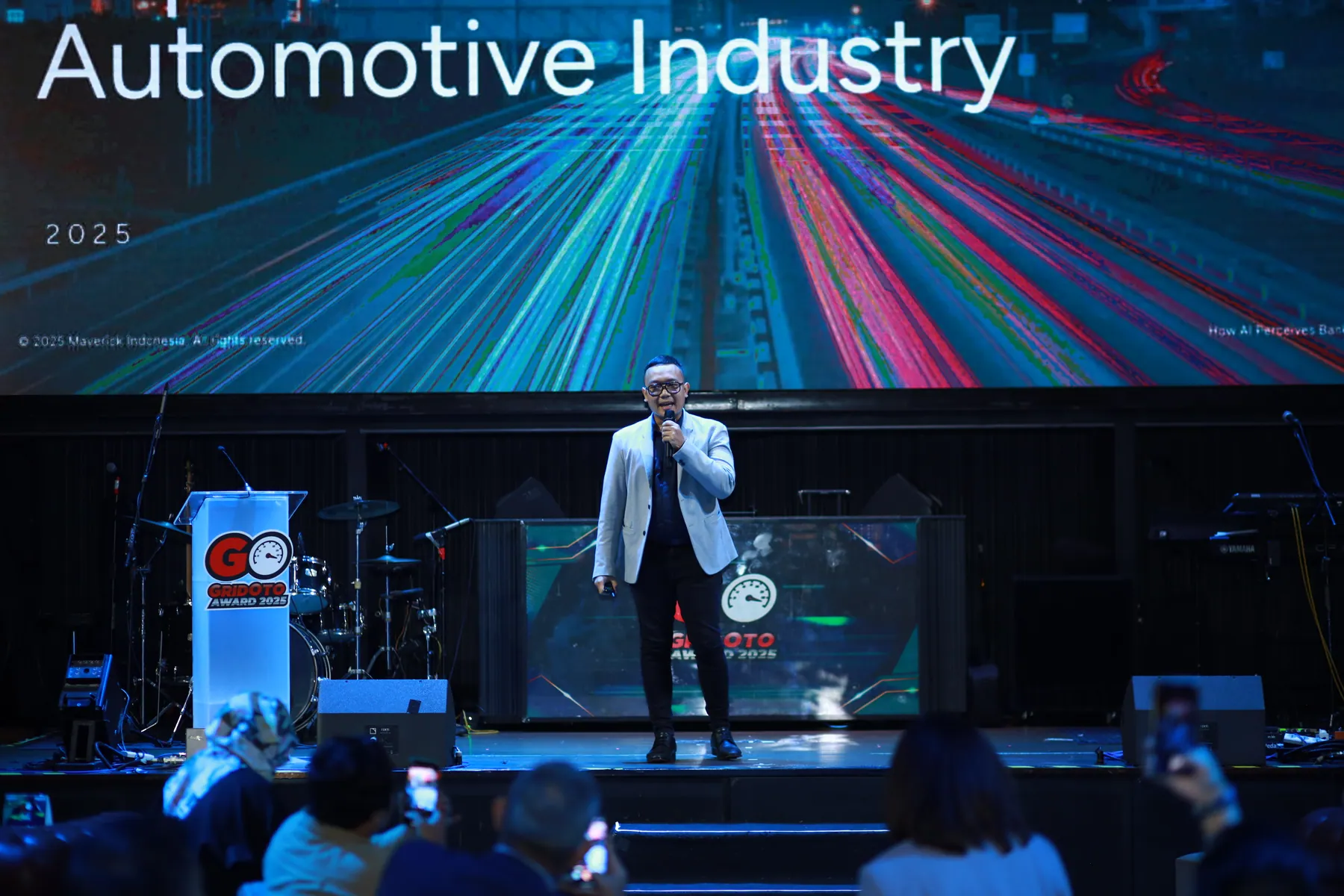 Cahyanto berbicara di panggung konferensi industri otomotif di depan layar presentasi.