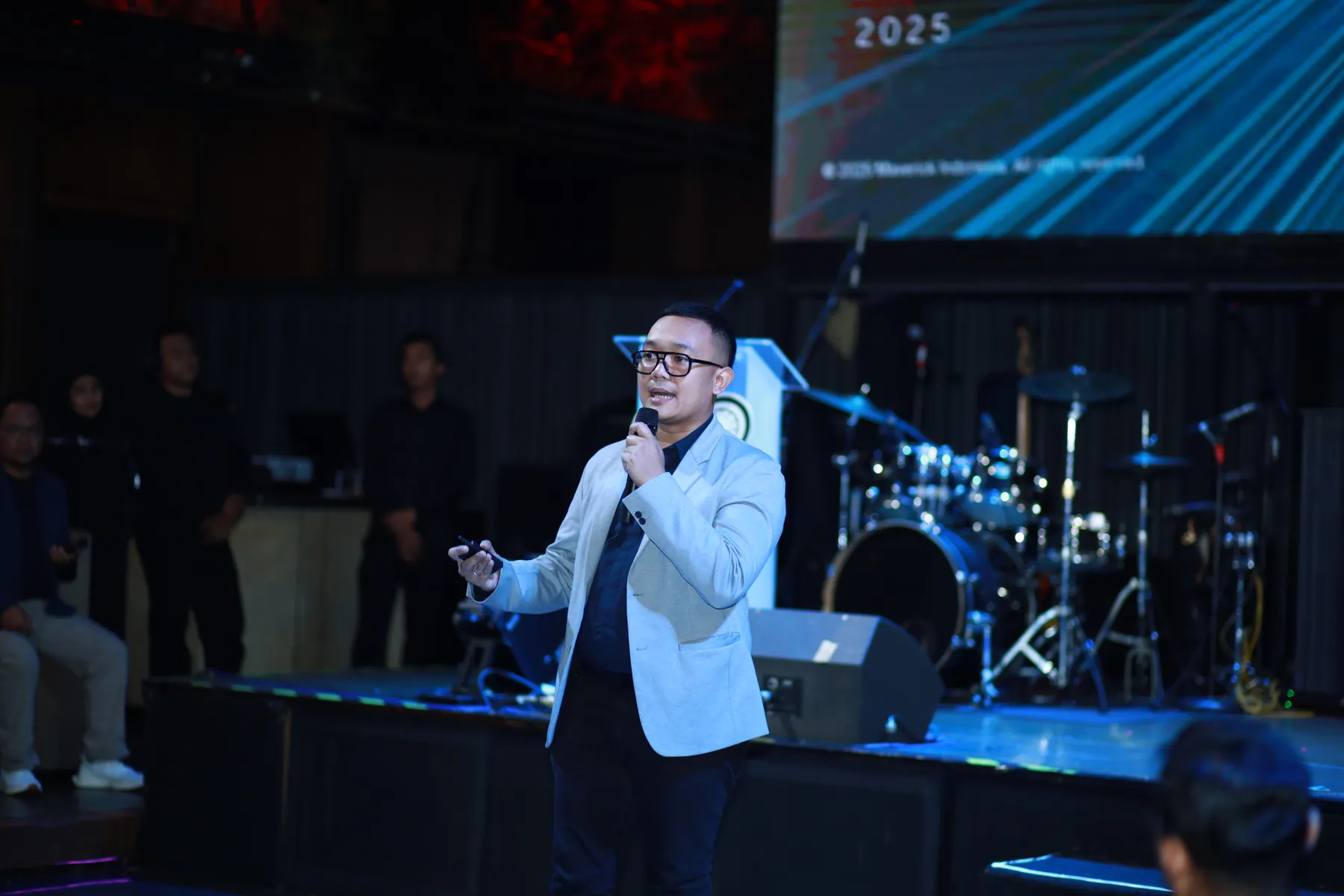 Cahyanto menyampaikan presentasi dengan mikrofon dan clicker di sebuah panggung.